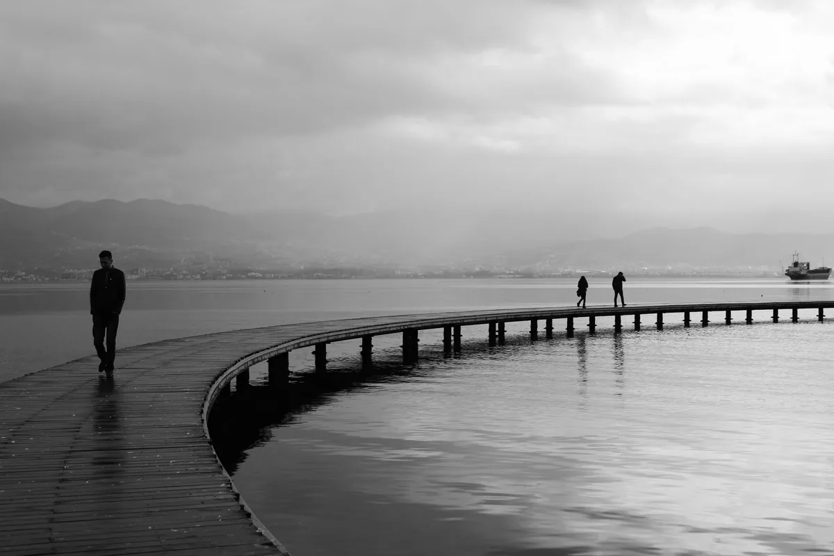 Por qué el trauma nos deja sin palabras: lo que la neurociencia revela sobre el cerebro "atrapado" 1 Hombre caminando solo por una pasarela sobre el mar en blanco y negro, imagen sobre cómo el trauma afecta al cerebro