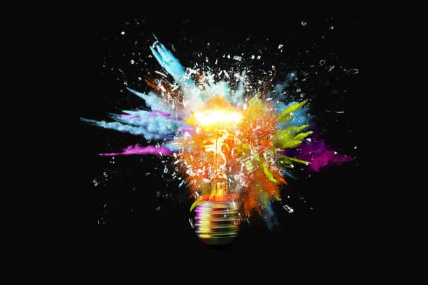 Síndrome del impostor en la era de la IA: ¿valgo menos si una máquina lo hace mejor que yo? 2 Bombilla que estalla en salpicaduras de pintura de colores y cristales sobre un fondo negro